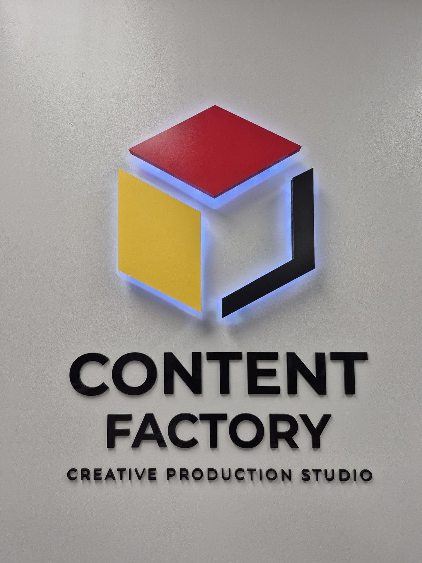 Halo-lit Content Factory cube logo sign glowing blue on a studio reception wall in Tampa